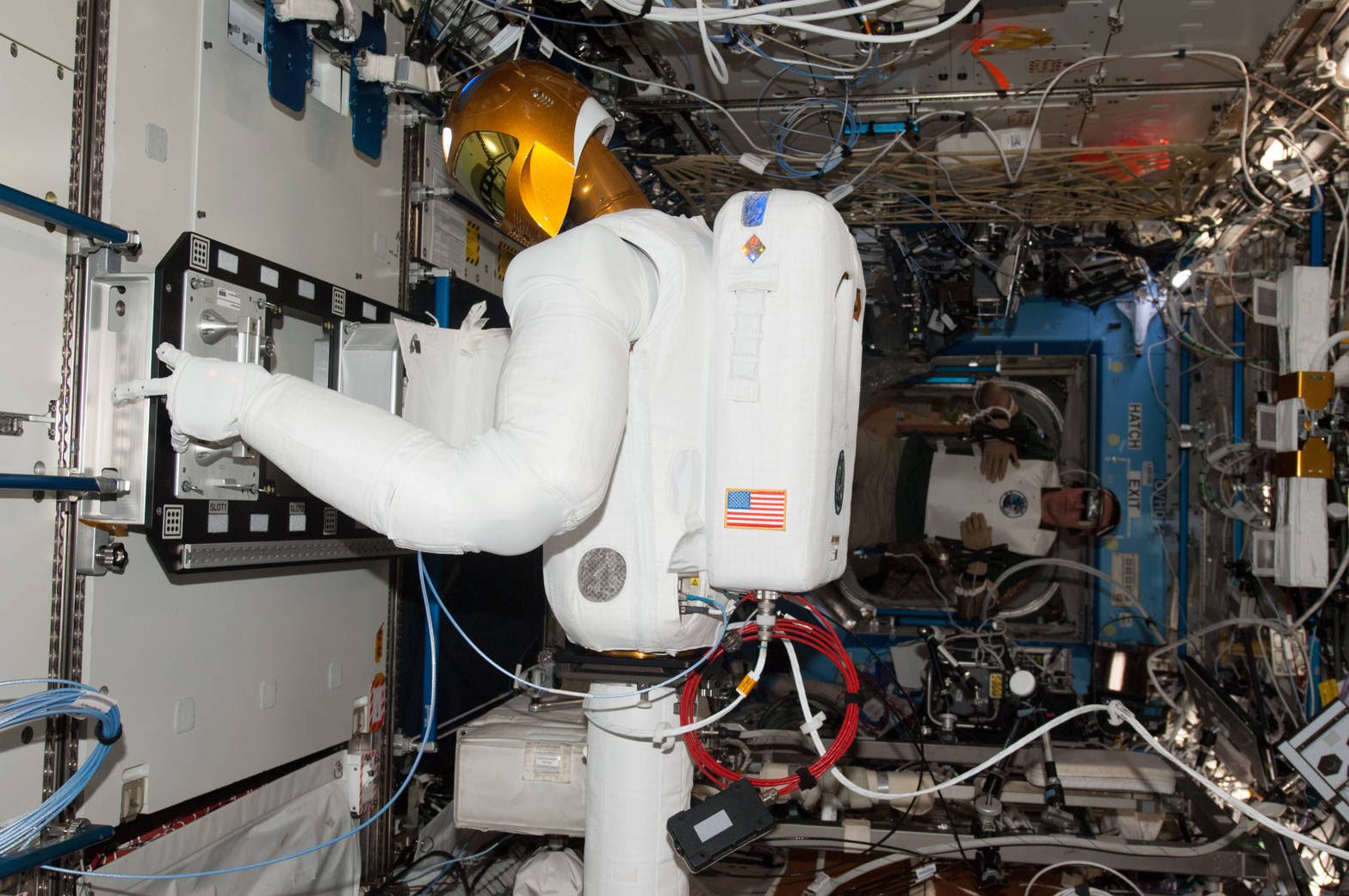 NASA astronaut with teleoperation equipment behind Robonaut 2 at a task board